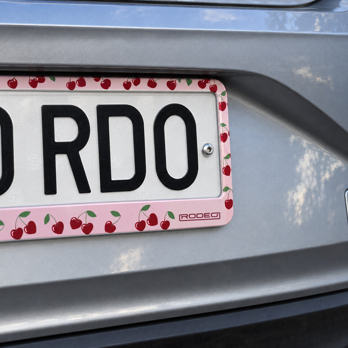 Detalle de las cerezas rojas y el logo Rodeo en la esquina del portamatrículas rosa.