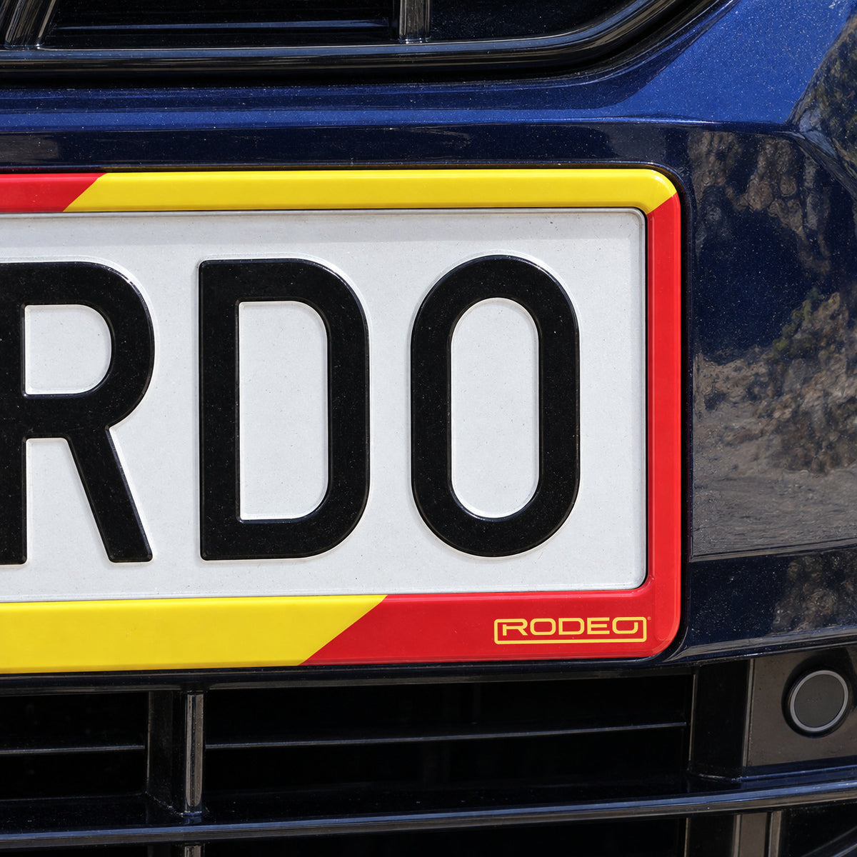 Detalle del logo Rodeo amarillo sobre la esquina roja del portamatrículas España Race.