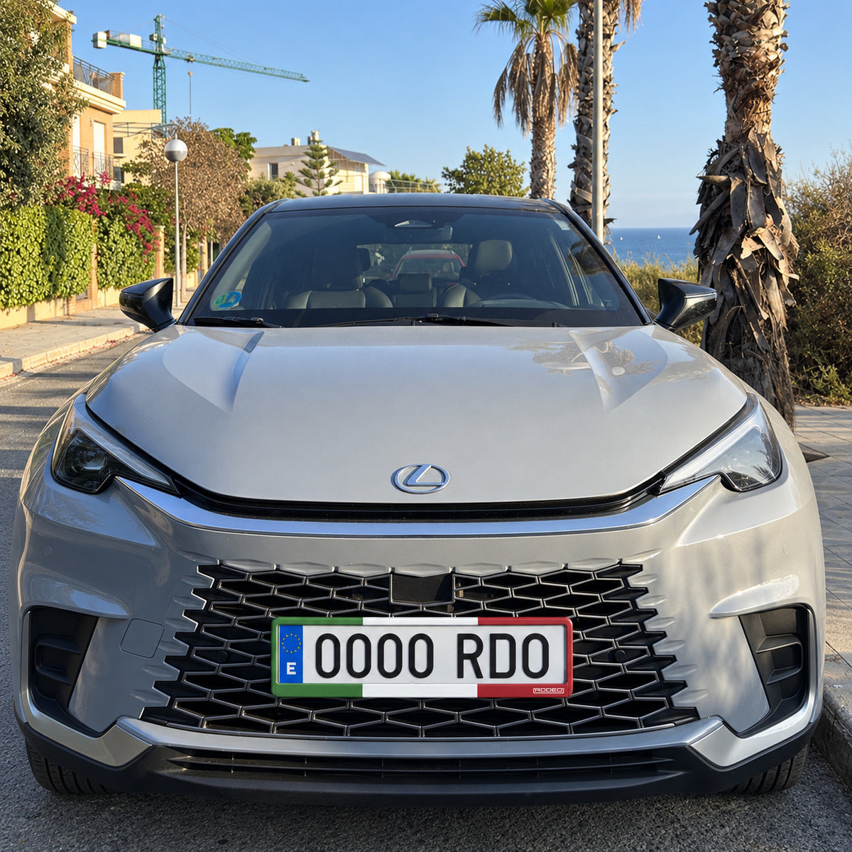 Portamatrículas Rodeo Italia instalado en la parte delantera de un Lexus LBX gris en una calle junto al mar.